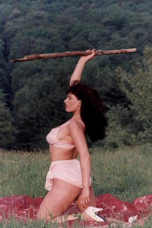 Woman Surrounded By Nature In Pink Lingerie & Heels Holding A Stick As A Weapon